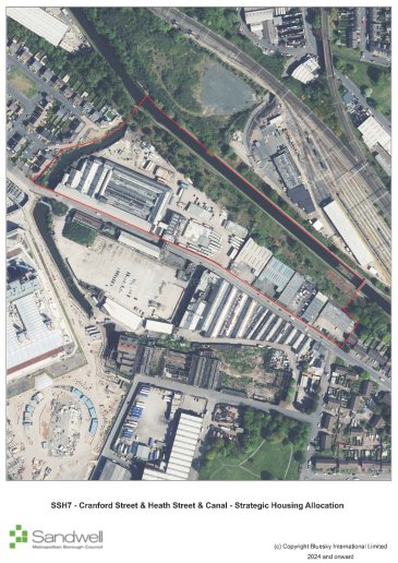 Aerial view of an urban area with a highlighted section along a canal and surrounding infrastructure, including buildings, railway lines, green spaces, and residential areas.