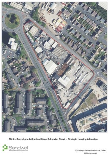 Outline boundary of a large urban area encompassing industrial buildings, warehouses, parking lots filled with vehicles, residential blocks, roads, and green spaces, with main roads intersecting the site.
