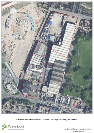 Aerial view of a site outlined in red, featuring multiple buildings, storage areas, and parking, adjacent to a park with green space on the right, a circular construction zone on the top left, and residential area at the bottom.