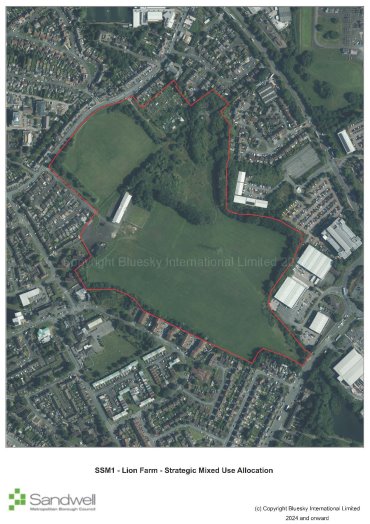 Aerial view of a park with an irregular red boundary line outlining the area, showing surrounding residential and industrial buildings, with green fields and trees within the boundary.