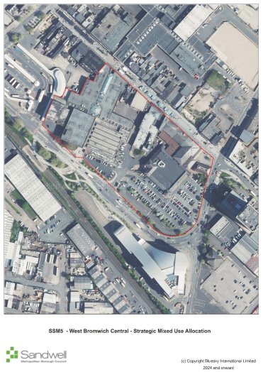 Aerial view of a developed urban area with buildings, roads, and parking lots, outlined in red indicating a specific designated zone.